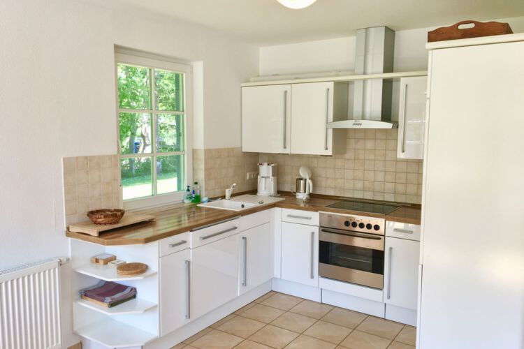 Offene geflieste Kueche im Erdgeschoss mit Geschirrspueler, Backofen, Ceranfeld, Kaffemaschine, Wasserkocher und Fenster mit Blick ins Gruene